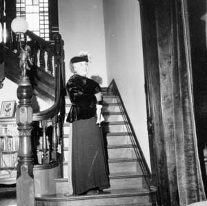 Woman in period dress on stairs, door to right is music room